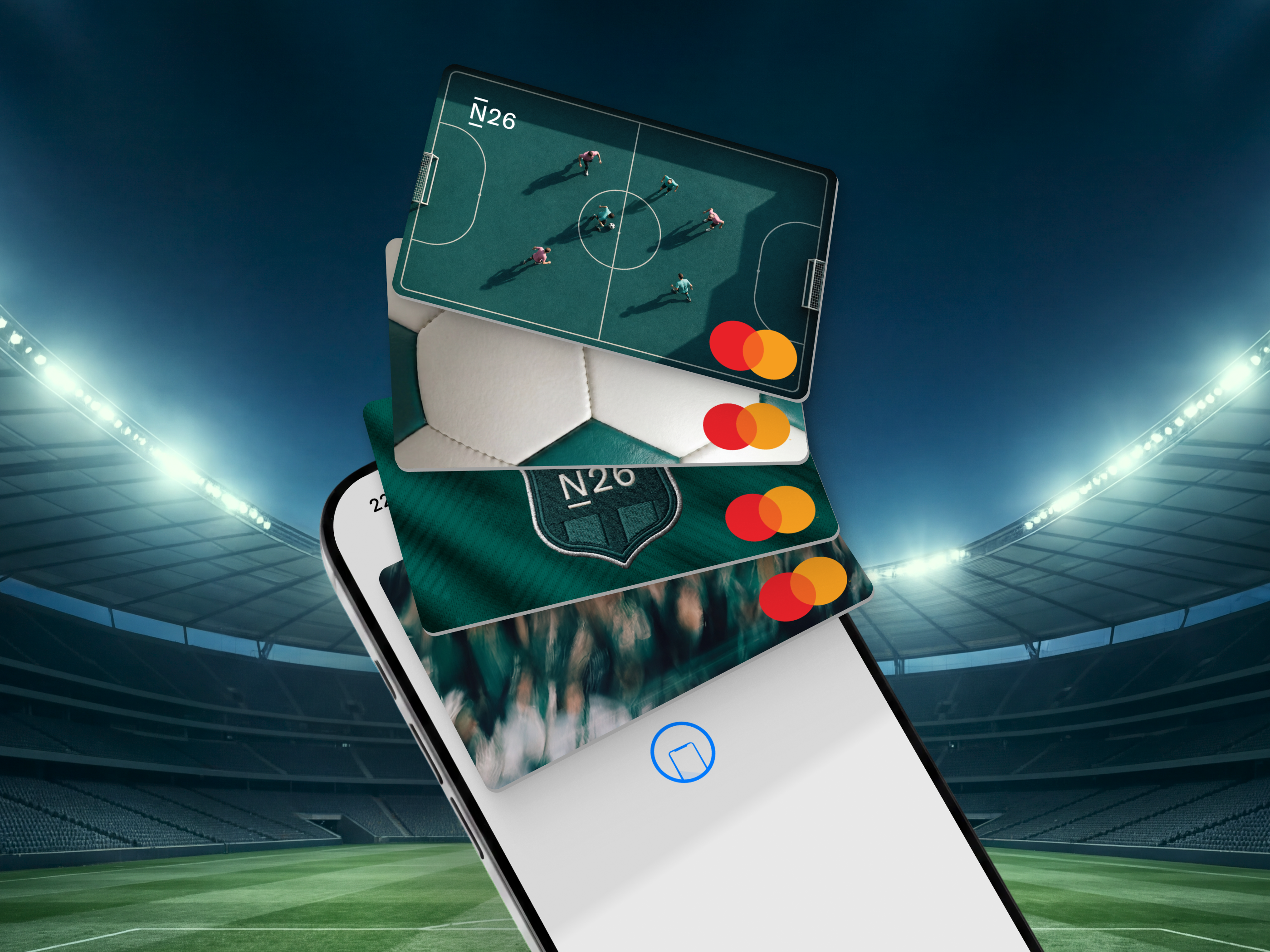 Auf einem Smartphone-Bildschirm ist ein fächerförmiger Stapel von vier virtuellen N26 Mastercard-Debitkarten mit Fußballmotiven vor dem Hintergrund eines verschwommenen Fußballstadions zu sehen.