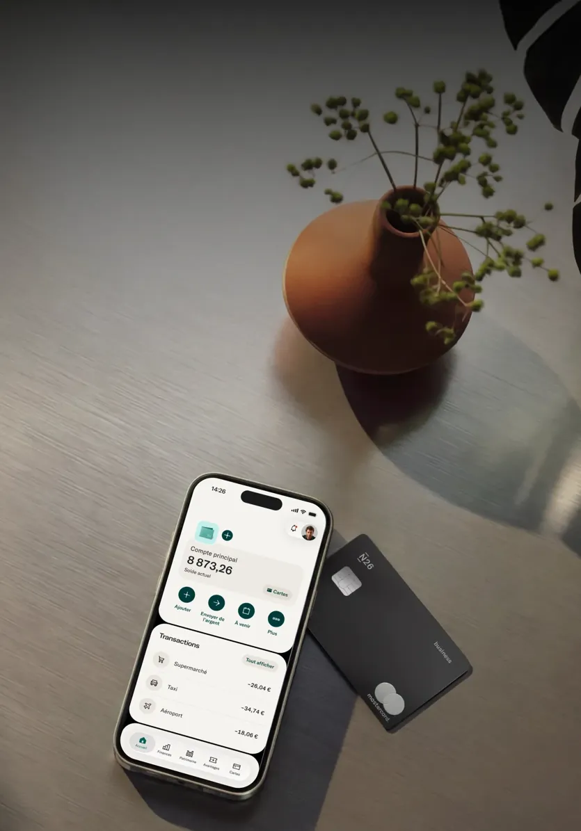 Un smartphone affichant une application bancaire repose sur une surface en bois à côté d'une carte bancaire en métal noire N26.