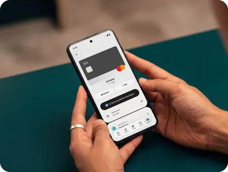 Eine Nahaufnahme von Händen, die ein Smartphone halten, auf dem die Benutzeroberfläche einer Banking-App angezeigt wird, eine virtuelle Karte und Optionen zum Hinzufügen der Karte zu einer mobilen Geldbörse darstellt.