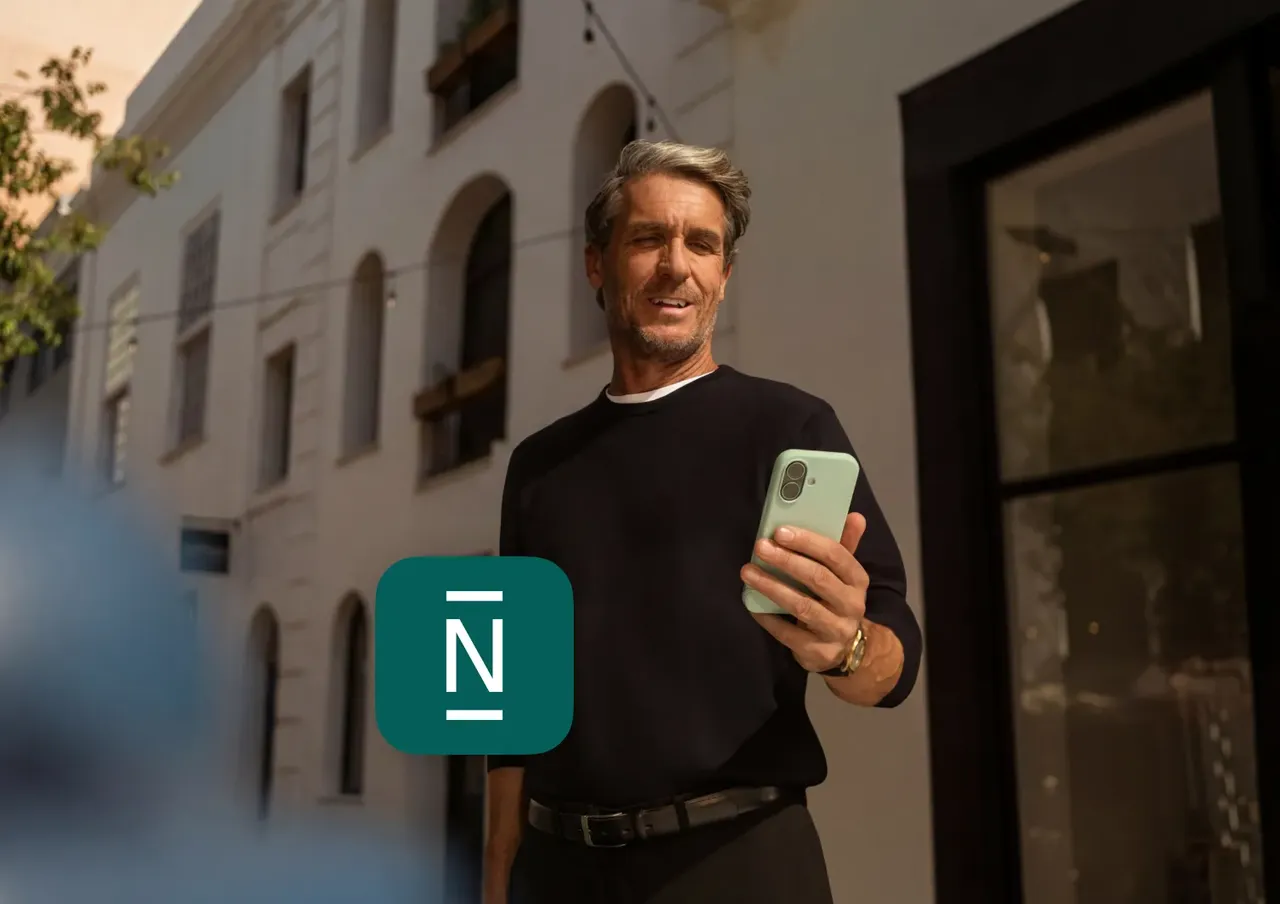 Ein mann im mittleren Alter in einem dunklen langärmligen Oberteil steht draußen vor einem Gebäude und blickt auf ein hellgrünes Smartphone in seiner Hand.