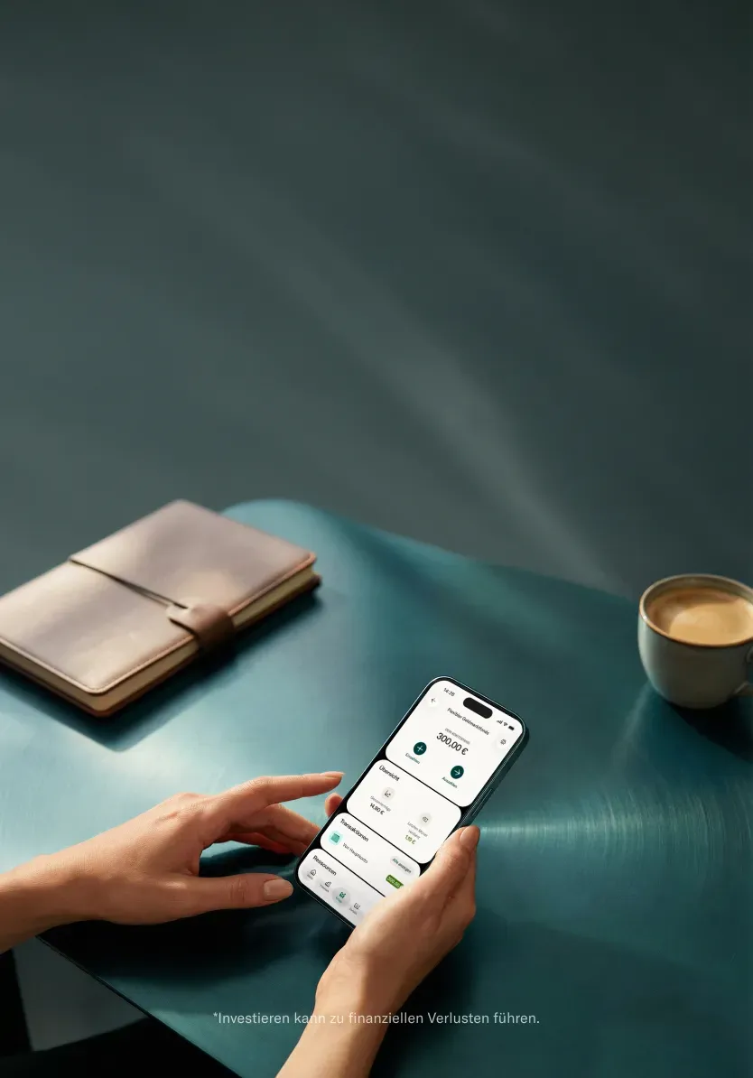 Eine Person hält ein Smartphone mit einer Finanz-App und einem Guthaben von 300,00 € neben einem Ledernotizbuch auf einem dunklen Tisch.