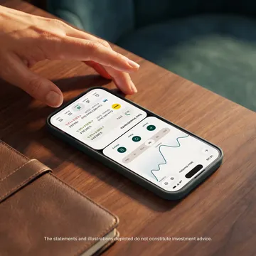 A hand rests near a smartphone on a wooden surface displaying an investment portfolio dashboard in an app interface.