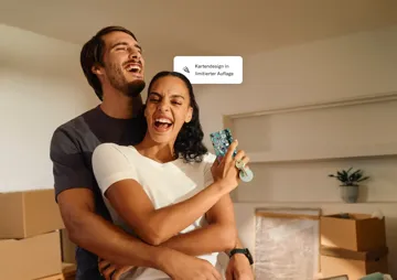 Ein lachendes junges Paar umarmt sich in einem Raum voller Umzugskartons, während die Frau eine bunte Kreditkarte und einen Schlüsselbund hochhält.