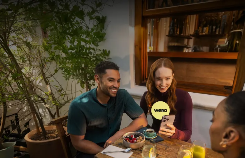 Ein Mann und eine Frau in einem Restaurant; die Frau hält ihr Handy und spricht mit einem Freund – mit einem WERO-Symbol.