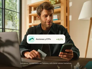 Un hombre está sentado frente a un escritorio sosteniendo una tarjeta de pago y un teléfono inteligente cerca de una computadora portátil, con un gráfico superpuesto que muestra "Stocks and ETFs" y un aumento del 6,2 %.
