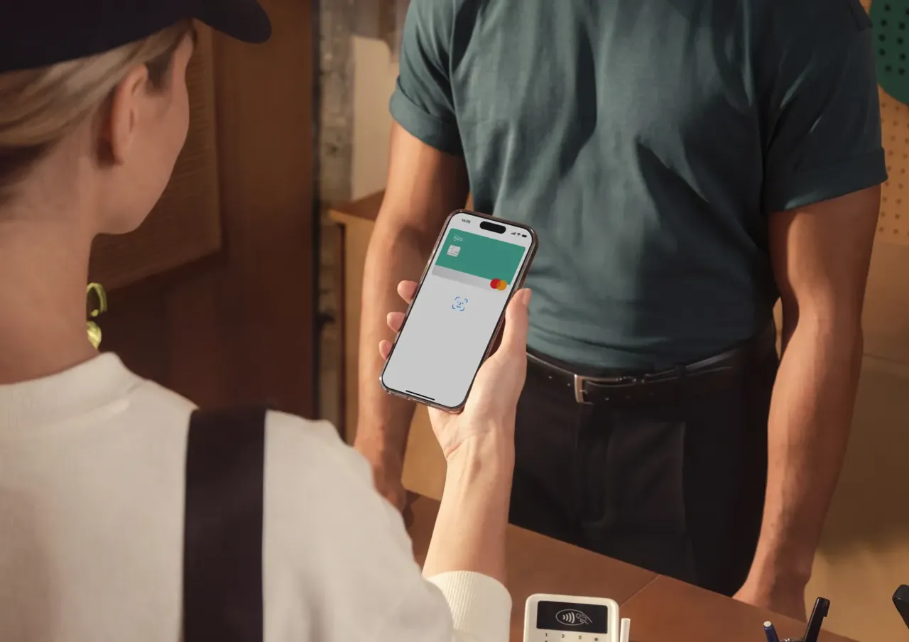 A person holds a smartphone near a payment terminal at a checkout counter to complete a contactless transaction.